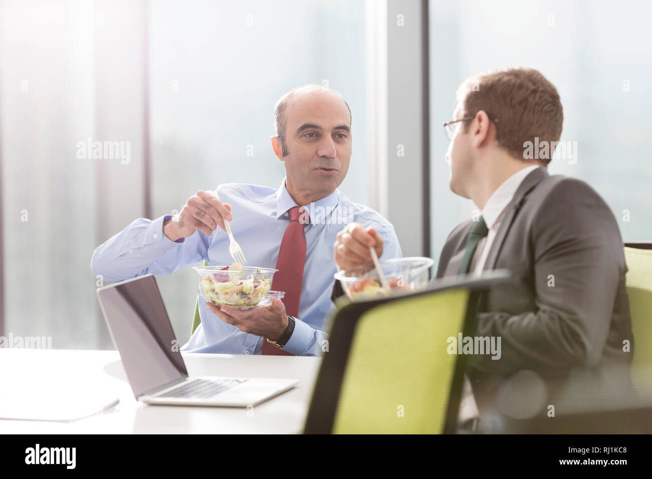 Unternehmer im Gespräch mit Kollegen, während das Mittagessen im Sitzungssaal während der Sitzung im Büro Stockfoto