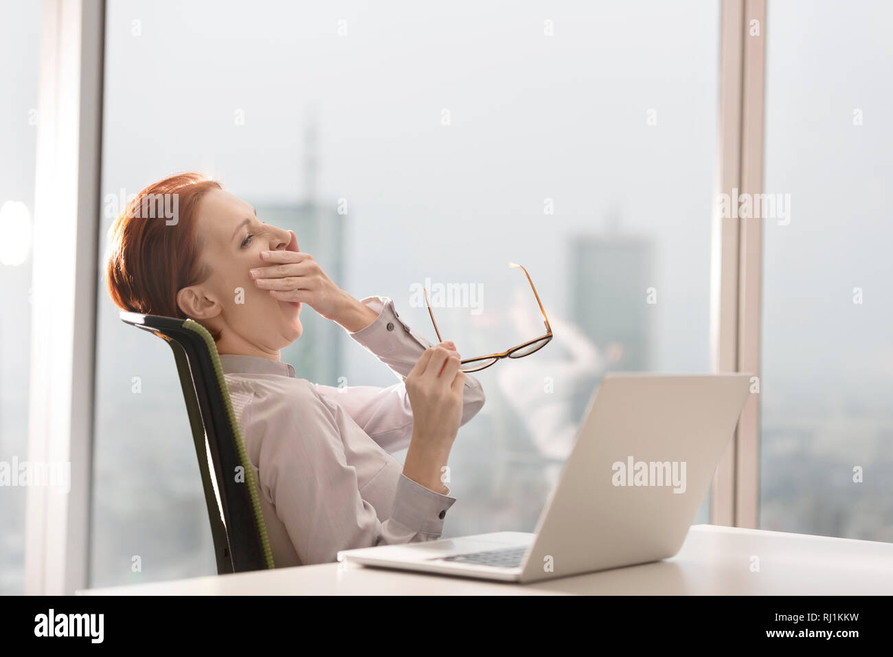 Müde junge geschäftsfrau Gähnen beim Sitzen mit Laptop auf dem Schreibtisch im Büro Stockfoto