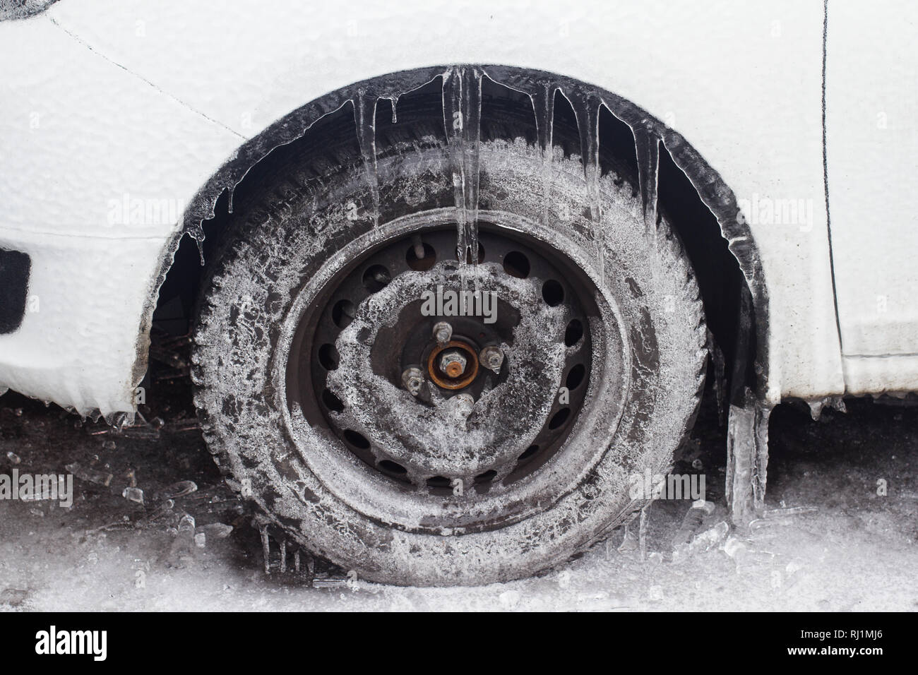 Seitenansicht Nahaufnahme des Weißen gefroren Auto mit gefrierendem Regen Eiszapfen an Reifen, die in einem Parkplatz im Schnee Winter Zeit gestoppt, hängend Stockfoto