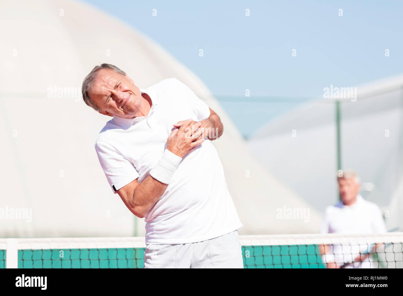 Ältere Menschen verziehen mit Schmerzen in der Brust, während sich gegen Freund während Tennis Match an einem sonnigen Tag Stockfoto