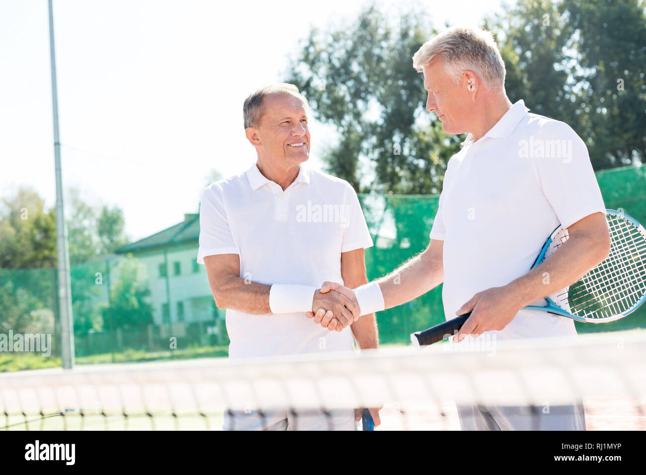 Lächelnde Männer Begrüßung beim Stehen auf Tennisplatz im Sommer überein Stockfoto