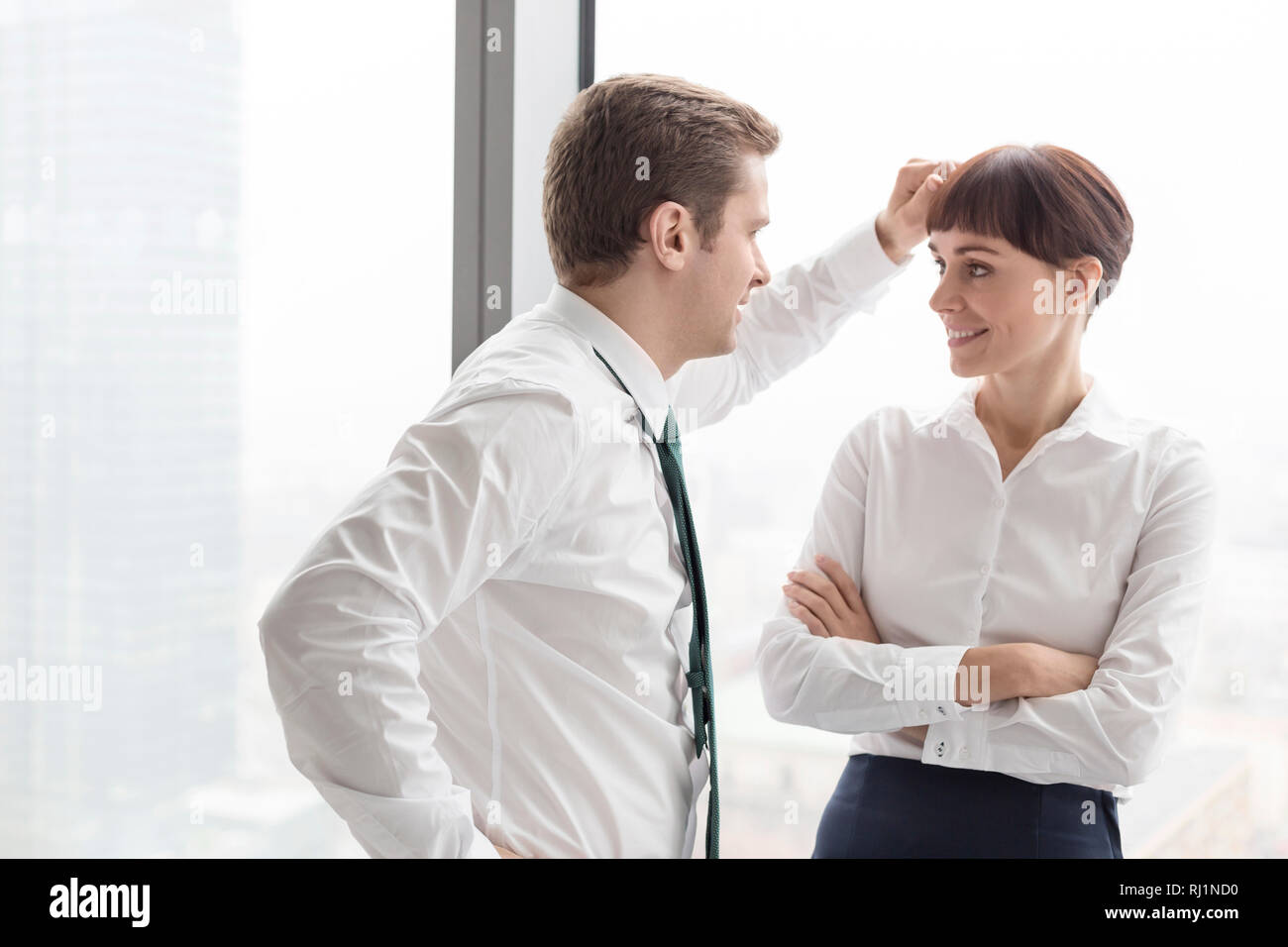 Geschäftsmann Flirten mit Geschäftsfrau stehend gegen Fenster im modernen Büro Stockfoto