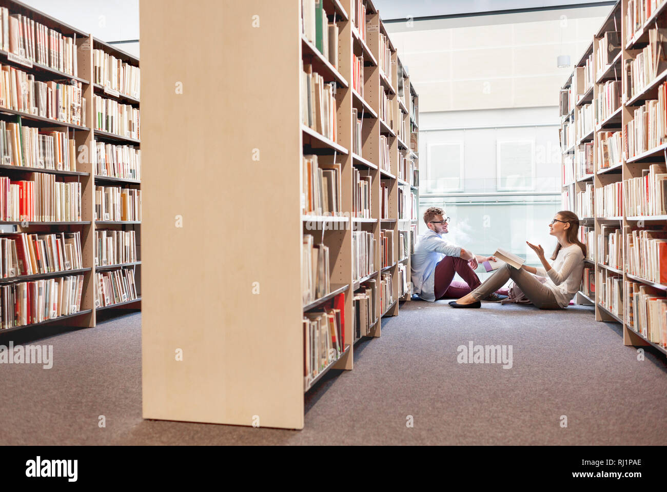 Mann und Frau diskutieren über buchen Sie beim Sitzen inmitten Regale an der Bibliothek Stockfoto