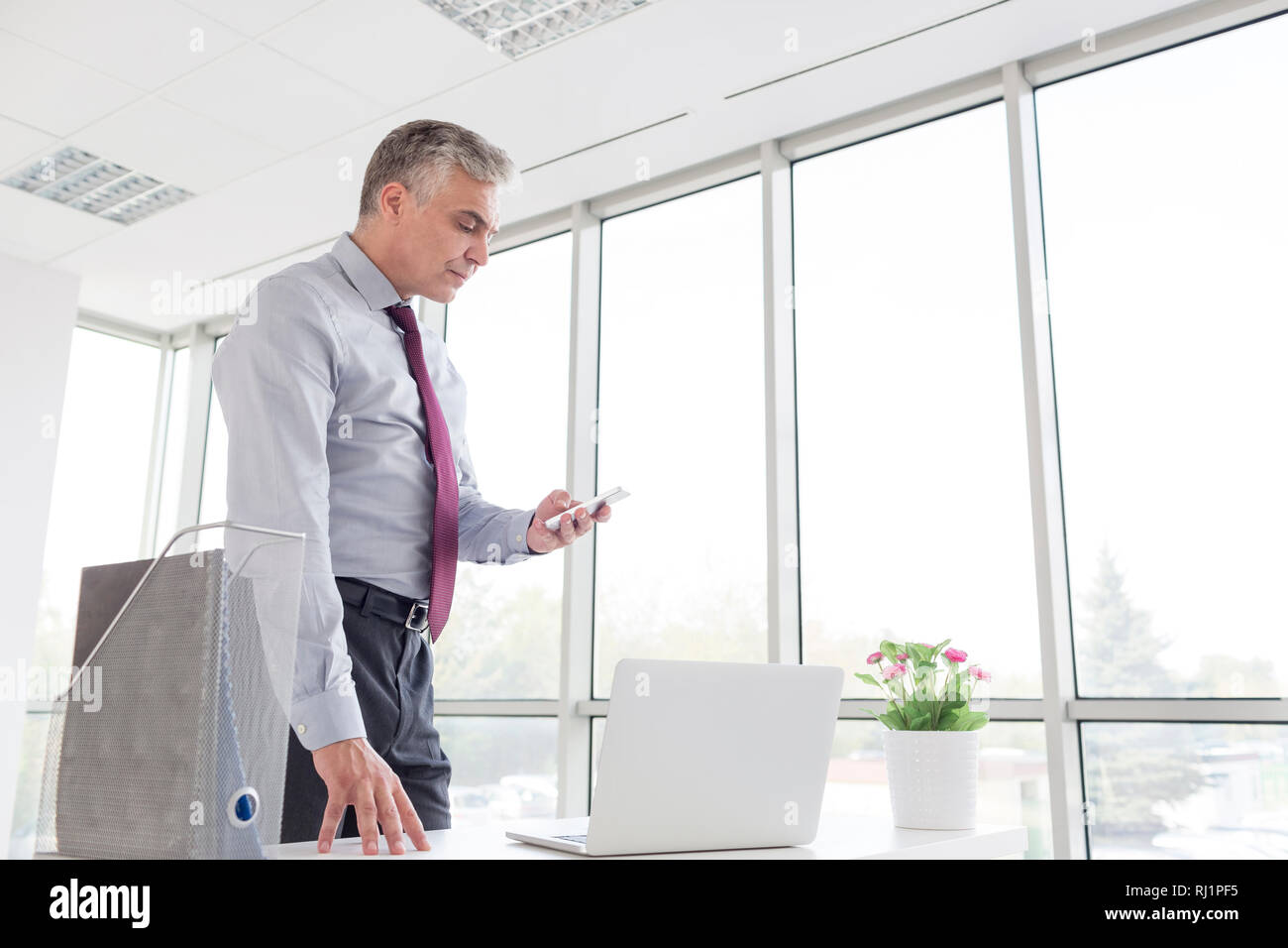 Reifen Geschäftsmann mit Smartphone, während am Schreibtisch stehen im neuen Büro Stockfoto
