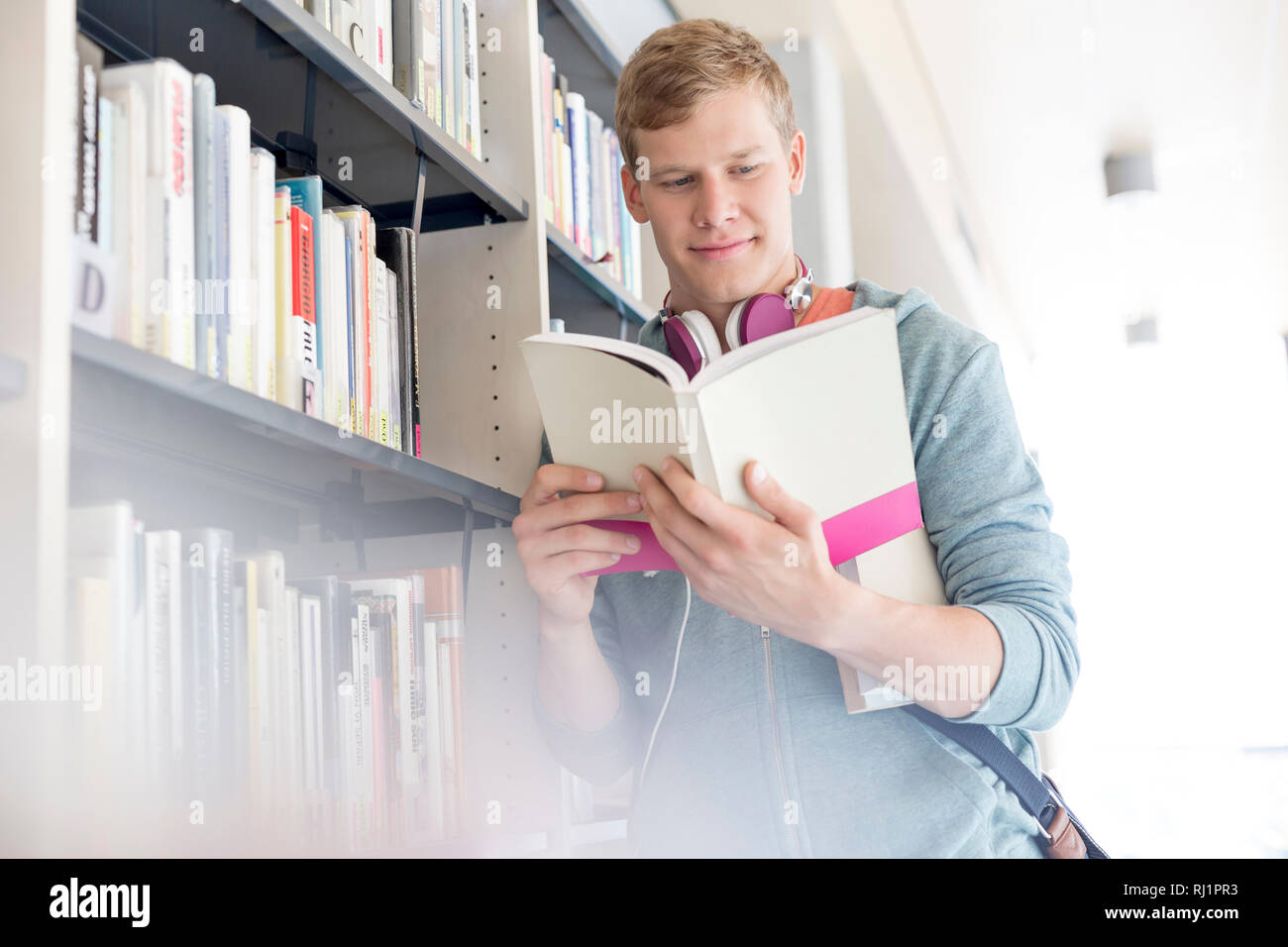 Lächelnd Schüler lesen Buch von Regal in der Bibliothek in der Universität Stockfoto