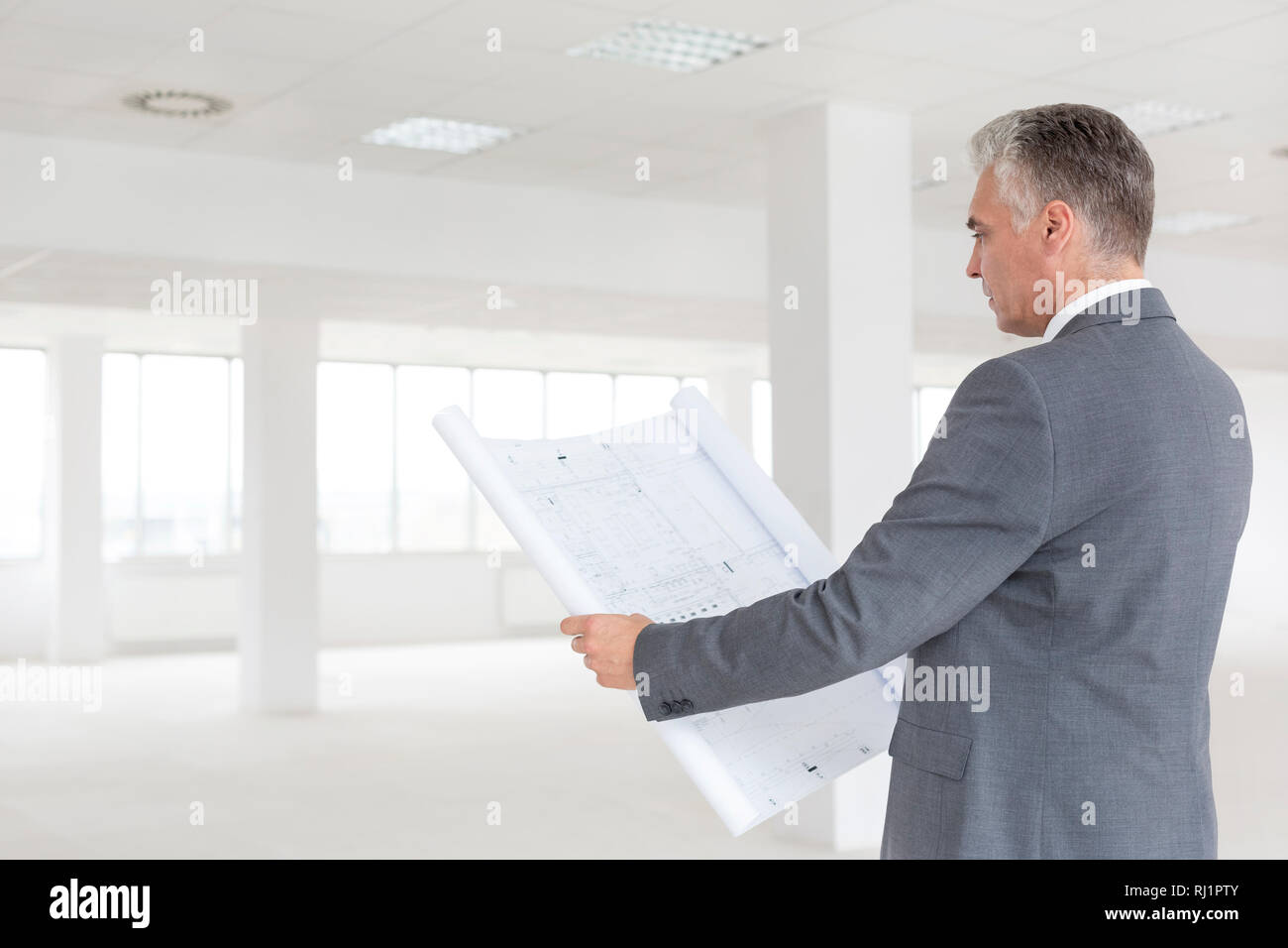 Reifen Geschäftsmann bei Blueprint Suche beim Stehen in der neuen leeren Büro Stockfoto