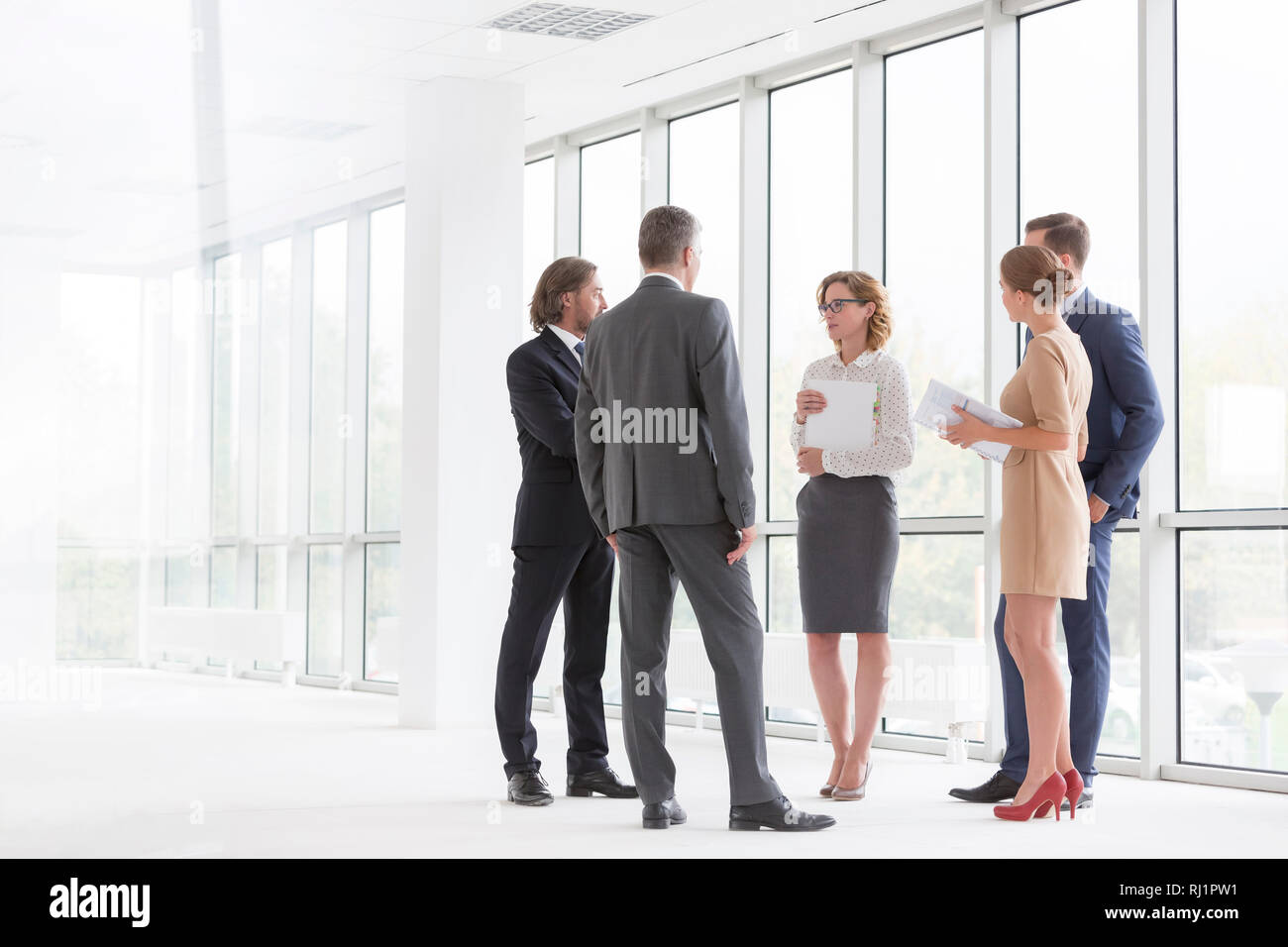 Kollegen diskutieren beim Stehen gegen Fenster im neuen Büro Stockfoto