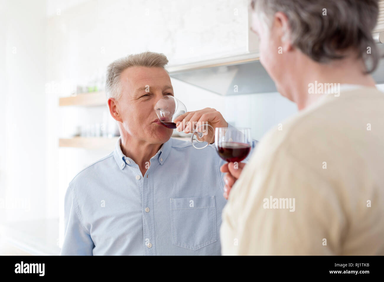 Reife Männer trinken Wein, während zu Hause stehend Stockfoto