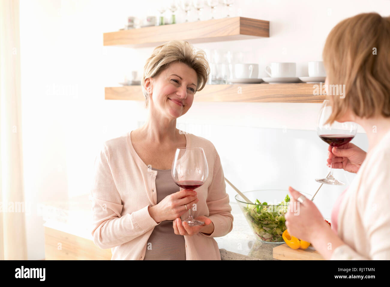 Ein Lächeln auf den Lippen reife Frauen halten Weingläser, während in der Küche stehend Stockfoto
