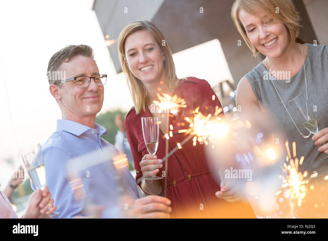 Lächelnd Kollegen holding Wunderkerzen und Weingläser während der Party auf dem Dach Stockfoto