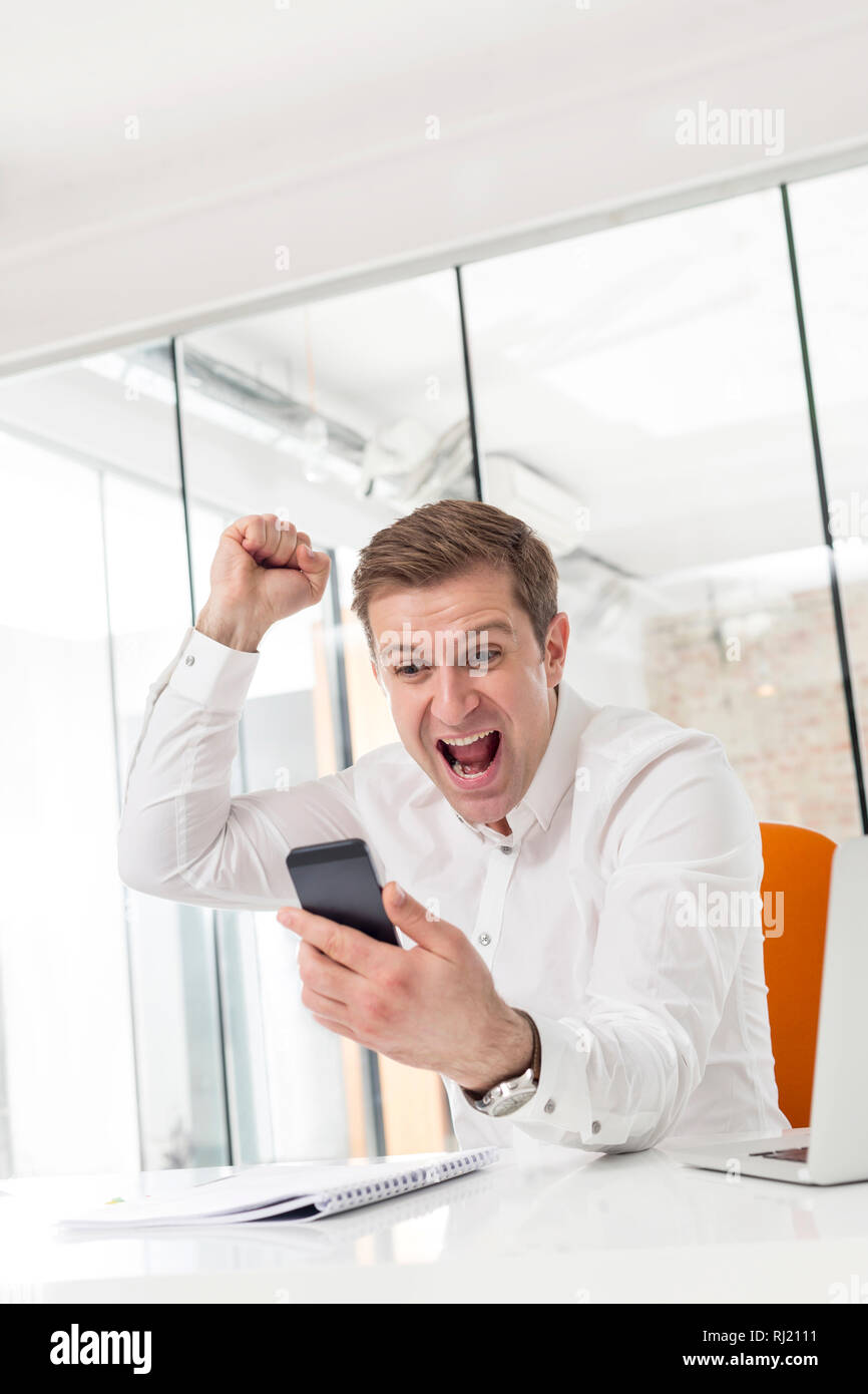 Kreative Unternehmer feiert Erfolg beim Smartphone im Büro suchen Stockfoto