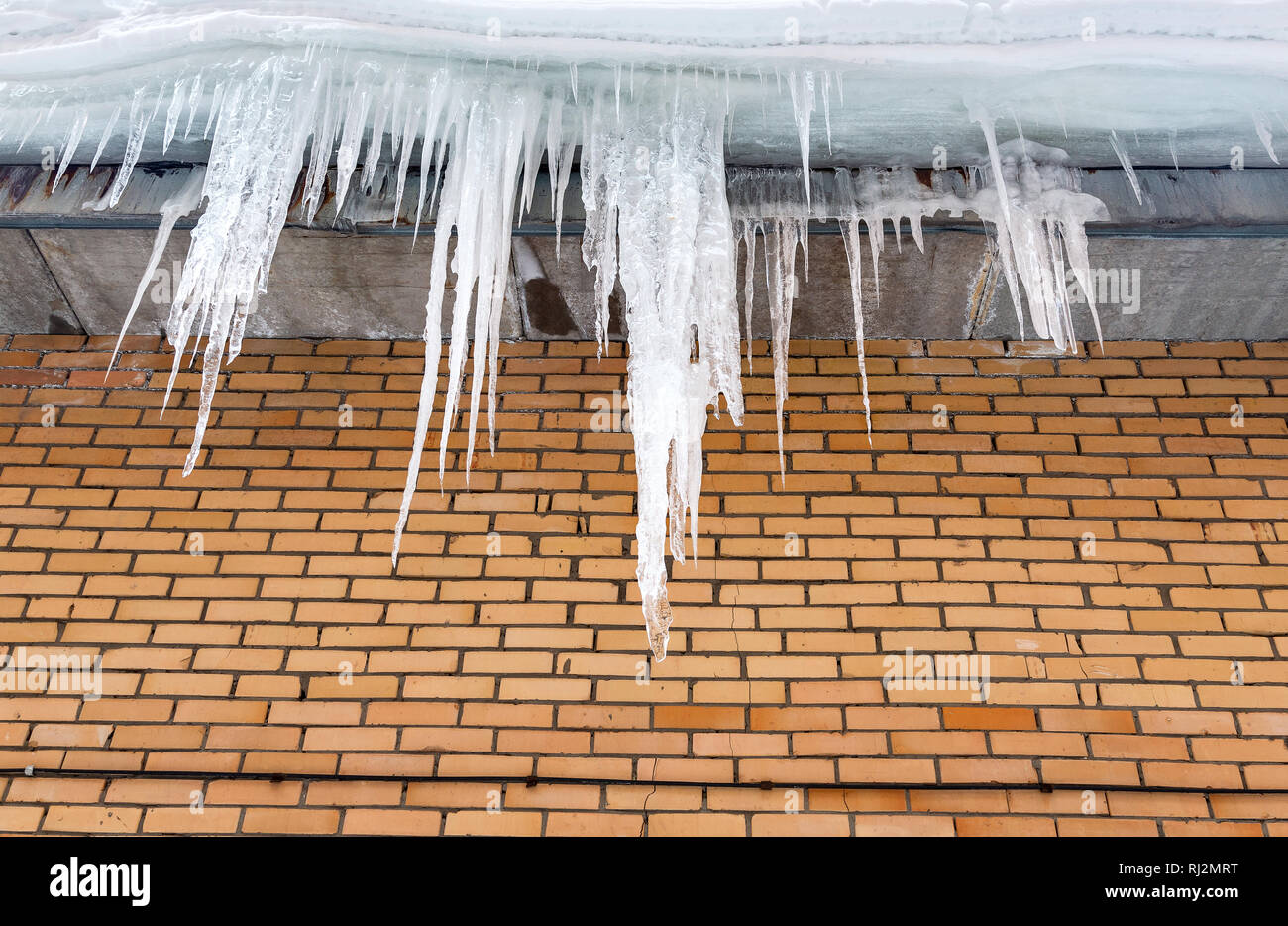 Transparente Eiszapfen auf dem Dach des Hauses im sonnigen Wintertag Stockfoto