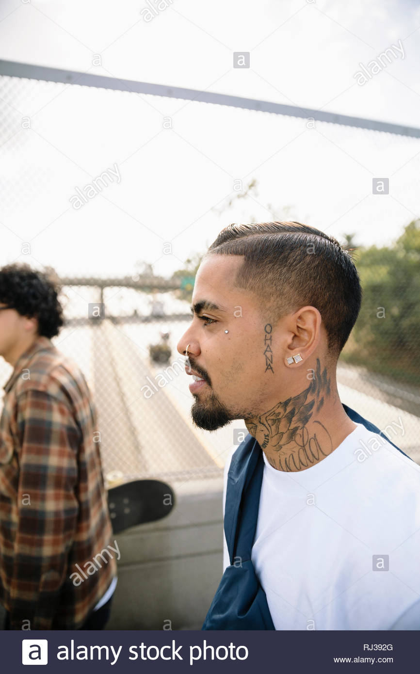 Latinx junger Mann mit Gesicht und Hals Tattoos entlang Überführung Stockfoto