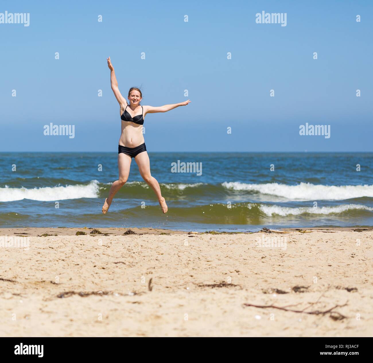 Glückliche junge Frau am Meer an der sonnigen Sommertag springen. Blonde Frau genießt die Feiertage. Stockfoto