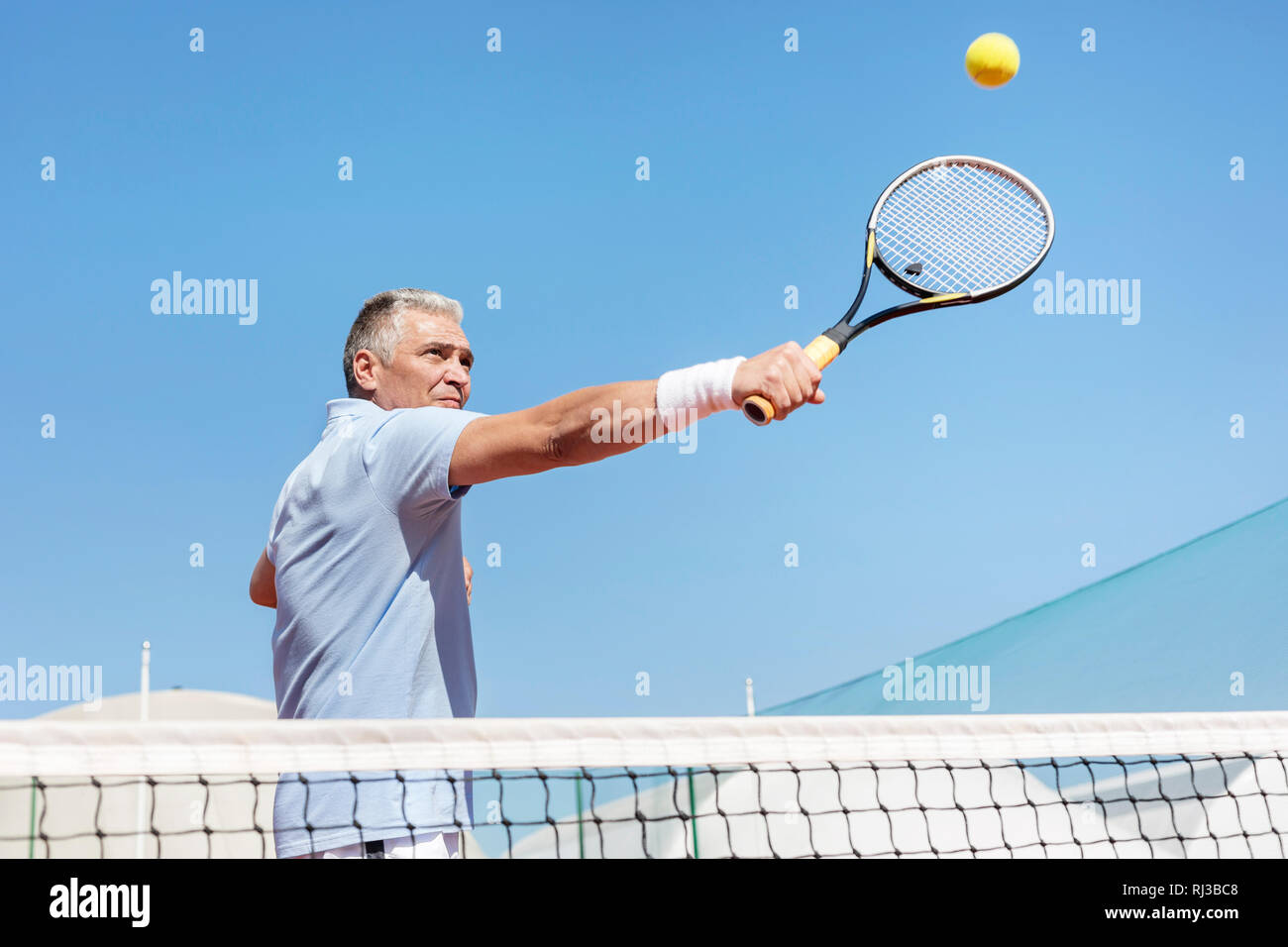 Low Angle View der Überzeugten reifer Mann schlagen Tennis ball mit Schläger auf Gericht gegen den klaren blauen Himmel Stockfoto