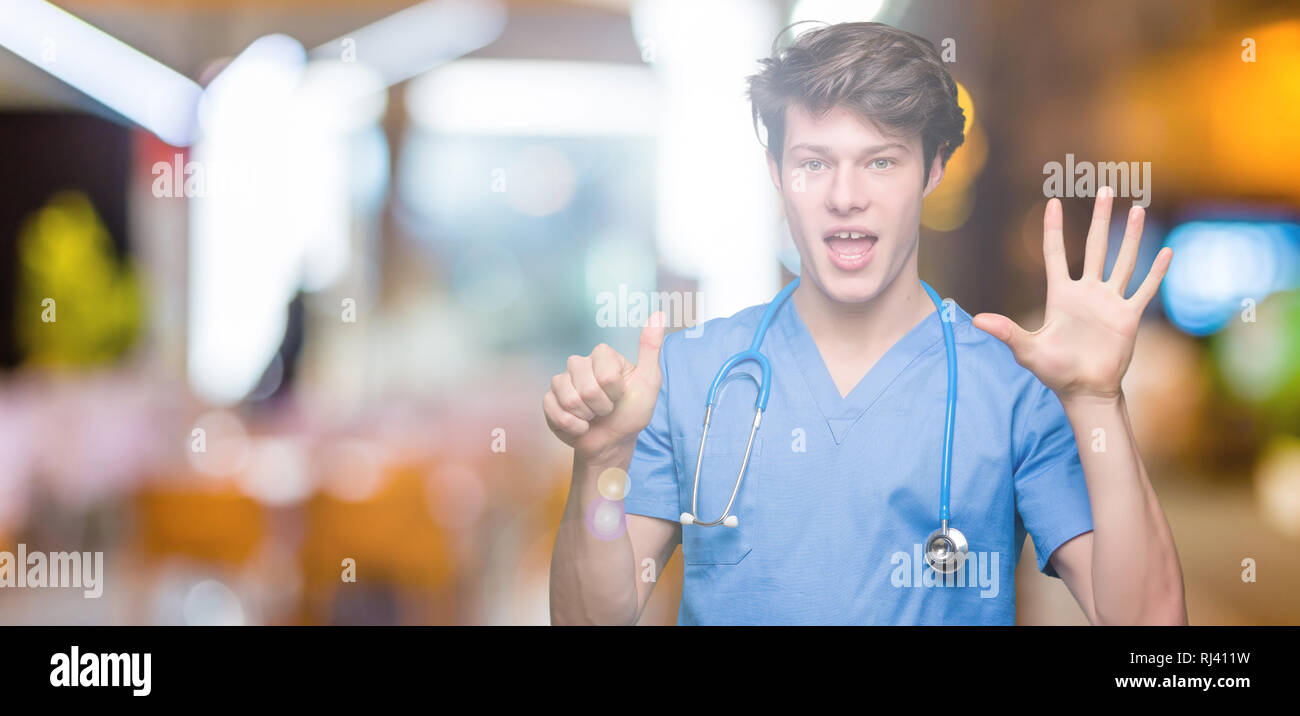 Junger Arzt mit medizinischen gleichmäßig über isolierte Hintergrund angezeigt und zeigen mit den Fingern Nummer sechs, während lächelte zuversichtlich und fröhlich. Stockfoto