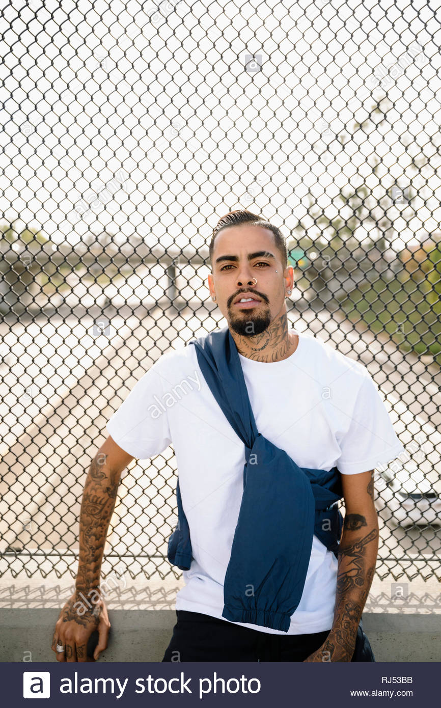 Portrait zuversichtlich, haltbare Latinx junger Mann mit Tätowierungen lehnte sich gegen Überführung Zaun Stockfoto