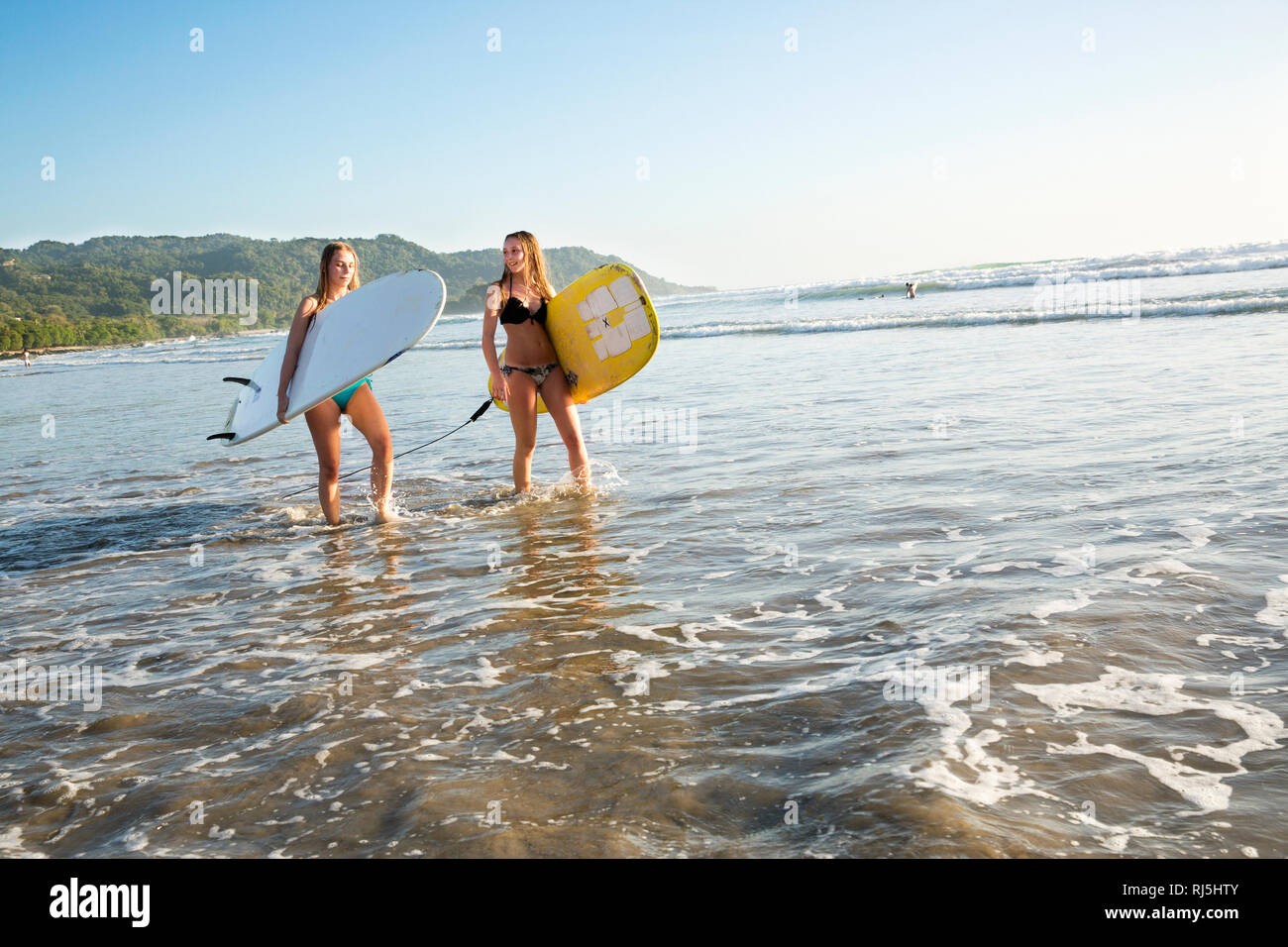 Zwei junge Frauen mit Surfboards Waten in Wasser Stockfoto