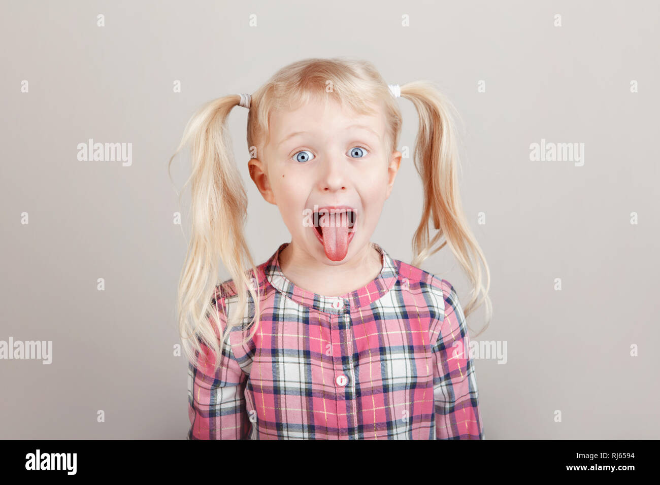 Closeup Portrait von Lustige blonde Kaukasischen Vorschule Mädchen, die Gesichter vor der Kamera. Kind mit Zunge auf normalem hellen Hintergrund. Kid Express Stockfoto