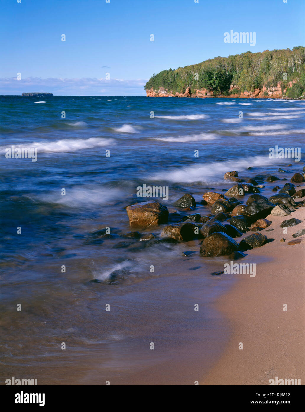 USA, Wisconsin, Apostel Islands National Lakeshore, Wellen am Lake Superior in Meyers Strand mit bewaldeten Landspitze und Eagle Island in der Ferne. Stockfoto