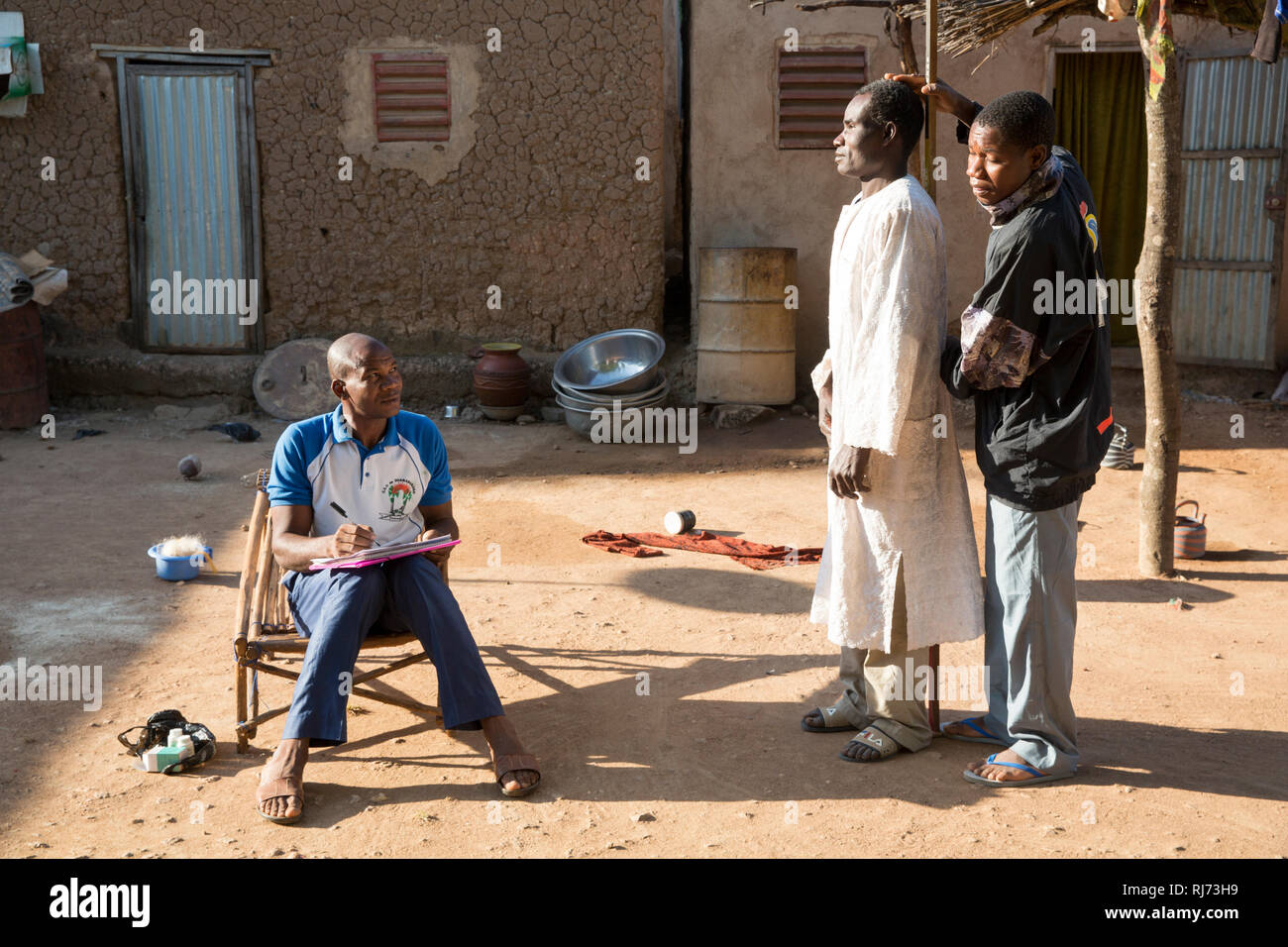 Diarabakoko-Dorf, Banfora, Cascades Region, Burkina Faso, 5. Dezember 2016; Soungalo Siri, Community Drug Distributor, mit dem Issouf Mande, Haushaltsvorstand, hat seine Höhe gemessen, um seine Dosis von Anti-Fluss-Blindheitsmedizin zu bestimmen. Stockfoto