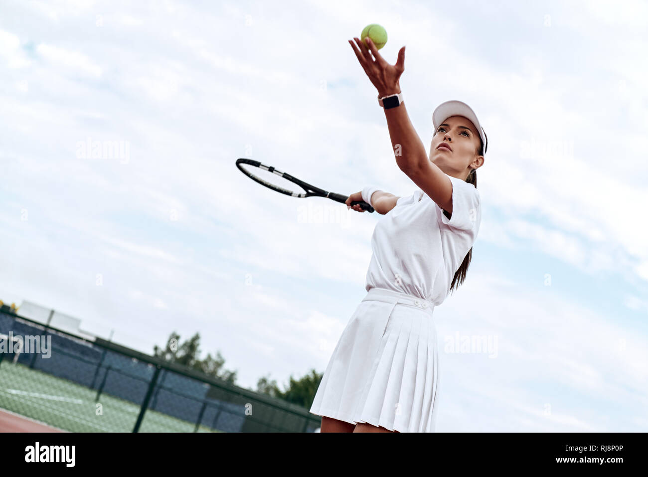 Attraktive Frau in Weiß Sportswear mit dem Schläger und dem Ball in der Hand ist bereit, den Ball auf dem Hof zu schlagen Stockfoto