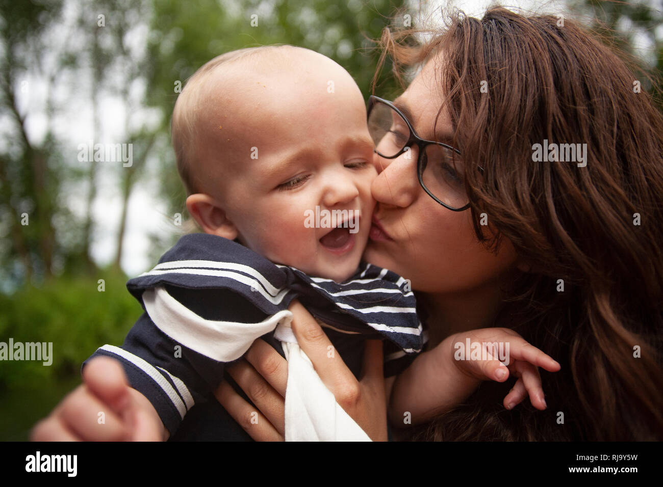 Eine junge Mutter liebt einen zärtlichen Moment, als sie ihr wertvolles Baby aufnimmt und Liebe mit einem süßen Kuss auf die Wange duscht. Stockfoto