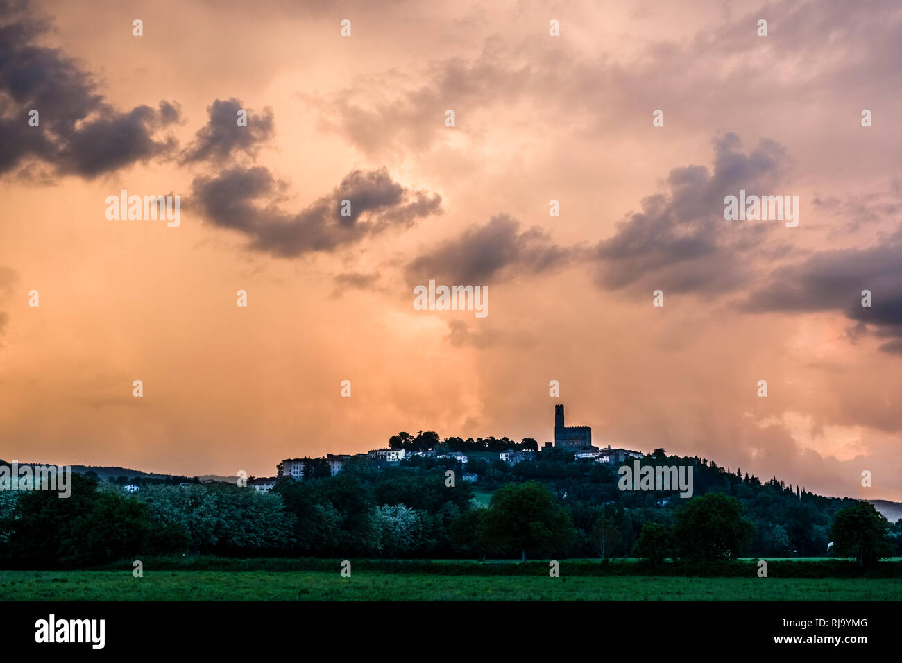 Typische hügelige toskanische Landschaft mit Feldern und Bäumen, die mittelalterliche Stadt auf einem Hügel bei Sonnenuntergang entfernt Stockfoto