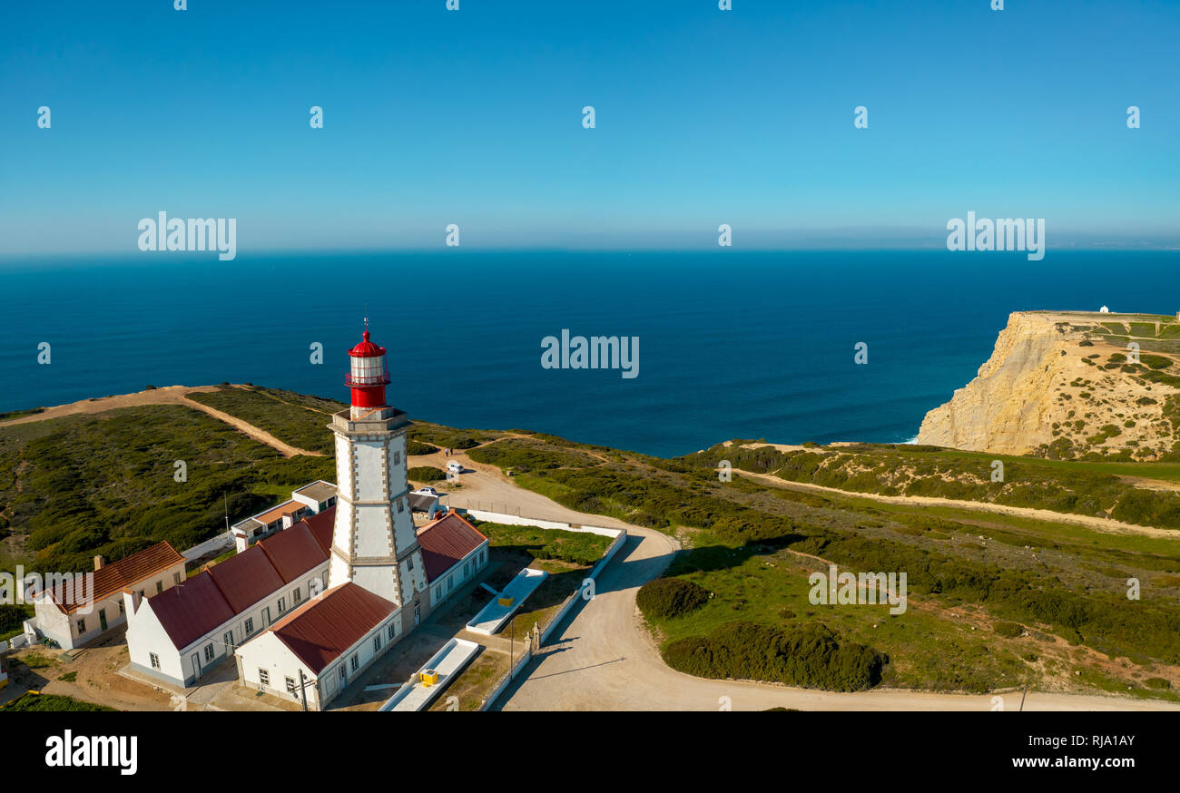 Antenne; drone Ansicht der weiß-roten Leuchtturm Cabo Espichel am Rande der Erde, türkisfarbenen Wasser des Atlantischen Ozeans erstreckt sich bis zum Horizont; schöne Stockfoto