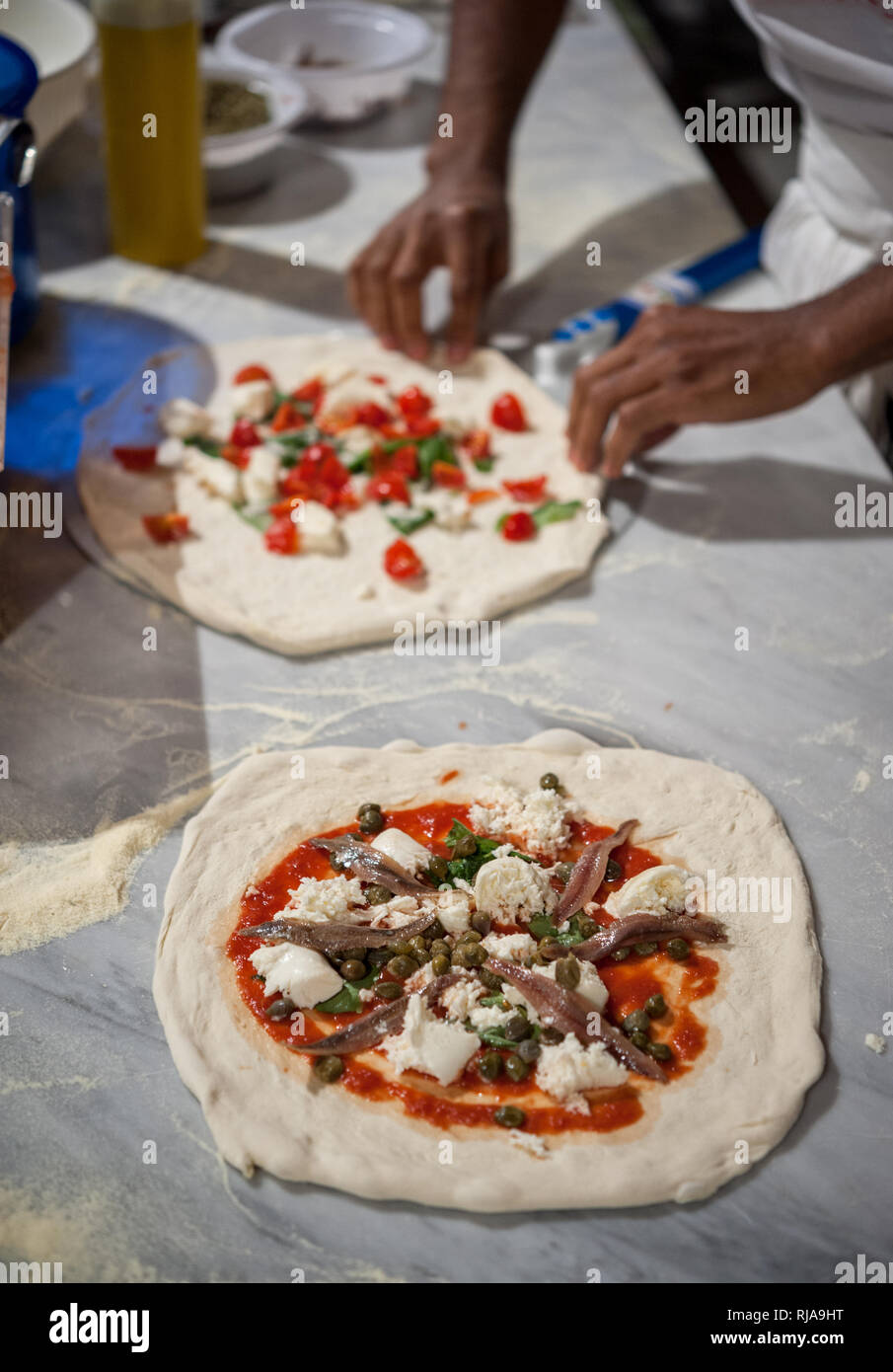Vorbereitung Pizza Margherita auf einem Ablageflächen aus Marmor. Neapolitanische Pizza, mit anchoives und Kapern, im Vordergrund. Selektiver Fokus Stockfoto