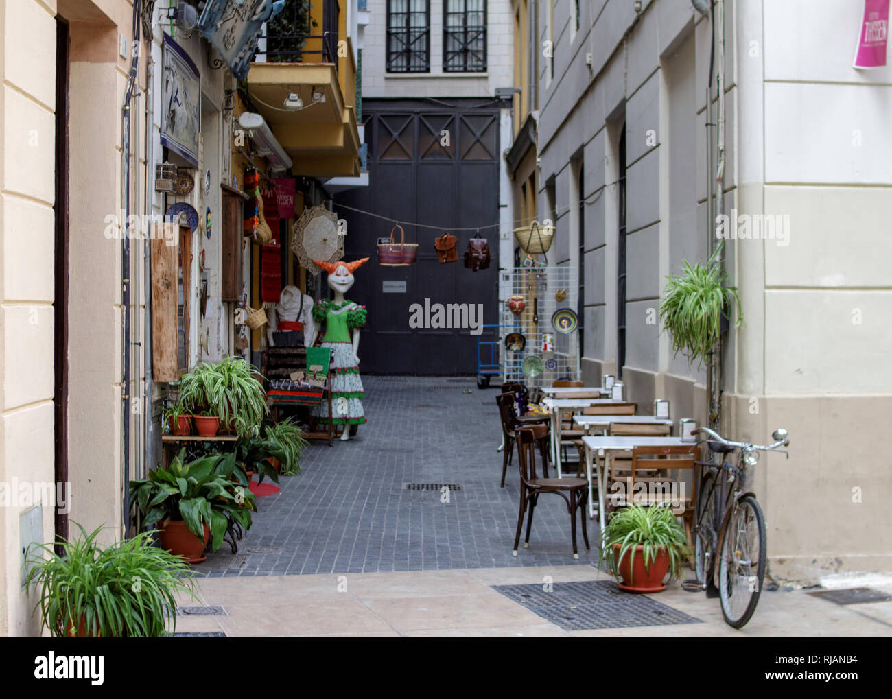 Malaga, Spanien. Eine kleine Seitenstraße in Malaga, Spanien mit Restauranttischen und einem Einzelhandelsgeschäft. Stockfoto