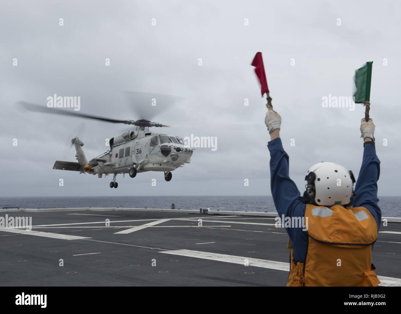 Pazifik (Nov. 4, 2016) - Flight Deck Besatzungsmitglieder Signale einer japanischen Maritime Self Defense Force SH-60K Hubschrauber für eine Landung an Bord des Japanischen Schiff (JS) Hyuga (DDH181) während der Übung scharfes Schwert 2017. Scharfes Schwert 17 ist ein gemeinsames und bilateralen Bereich Training (Ftx) zwischen US-amerikanischen und japanischen Truppen bedeutete die Bereitschaft und die Interoperabilität im Rahmen des U.S.-Japan Alliance zu erhöhen. Stockfoto