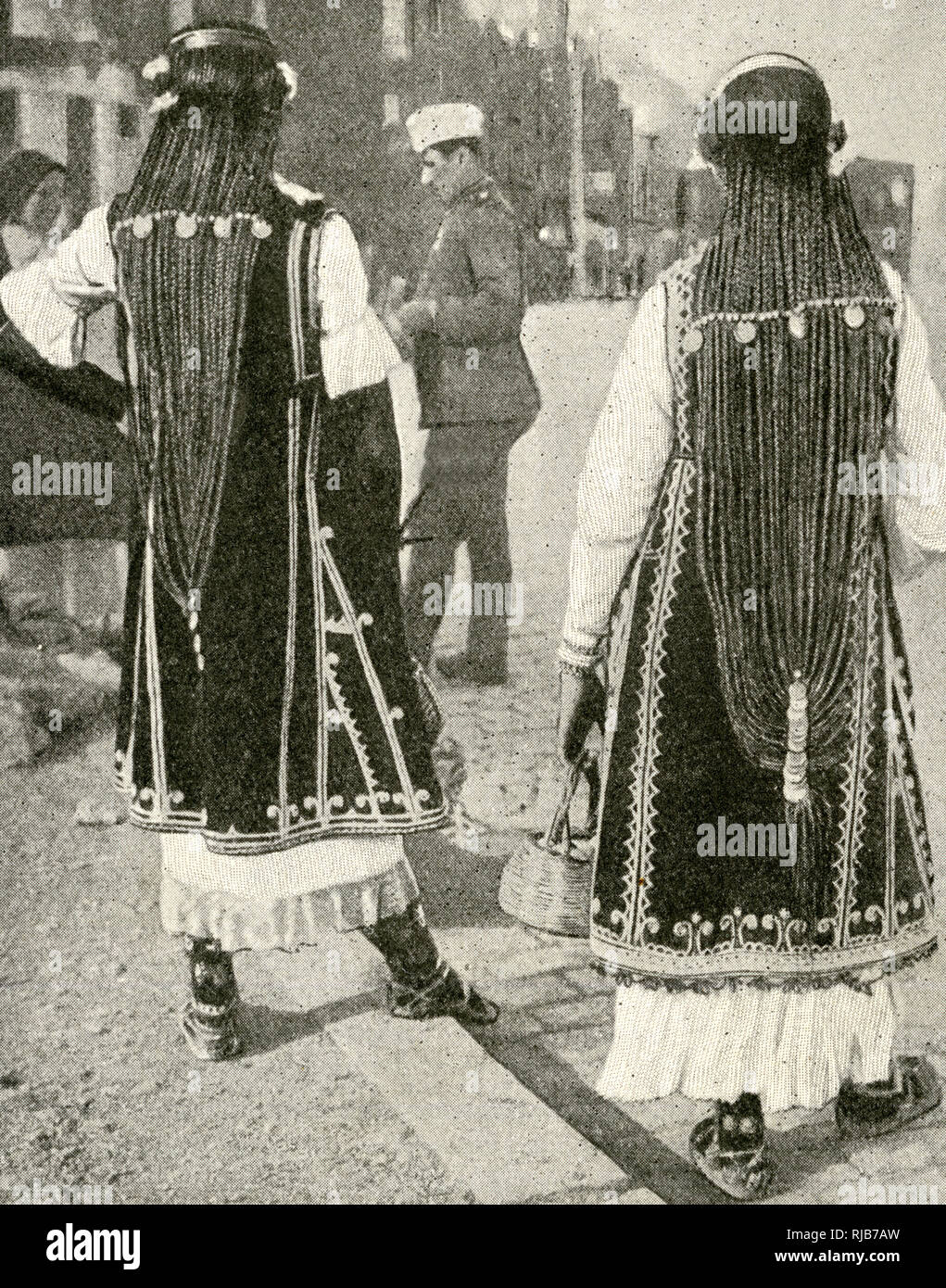 Zwei junge Frauen in traditioneller Kleidung in einem bulgarischen Straße, mit langen geflochtenen Haaren und Münze Dekorationen. Stockfoto