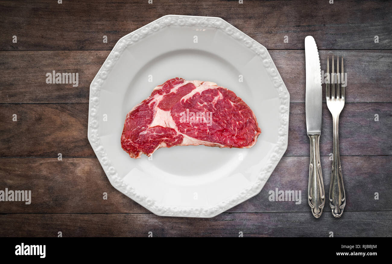 Rotes Fleisch/raw Steak auf dem Teller auf Holzuntergrund mit Messer und Gabel Stockfoto