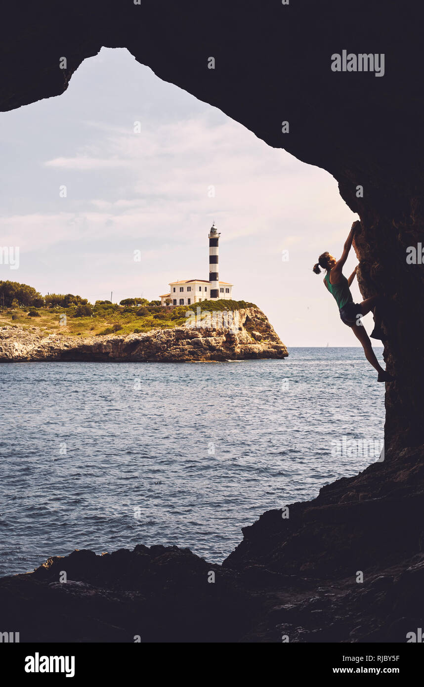 Silhouette einer Frau klettern in einer Höhle, Portocolom Leuchtturm im Hintergrund, Farbe Tonen angewendet, Mallorca, Balearen, Spanien. Stockfoto