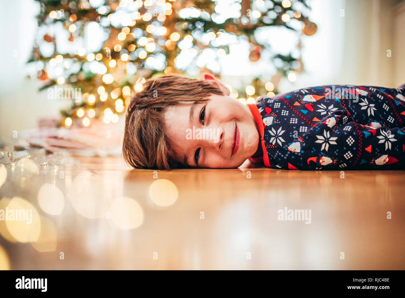 Lächelnde Junge lag auf dem Boden vor einem Weihnachtsbaum Stockfoto