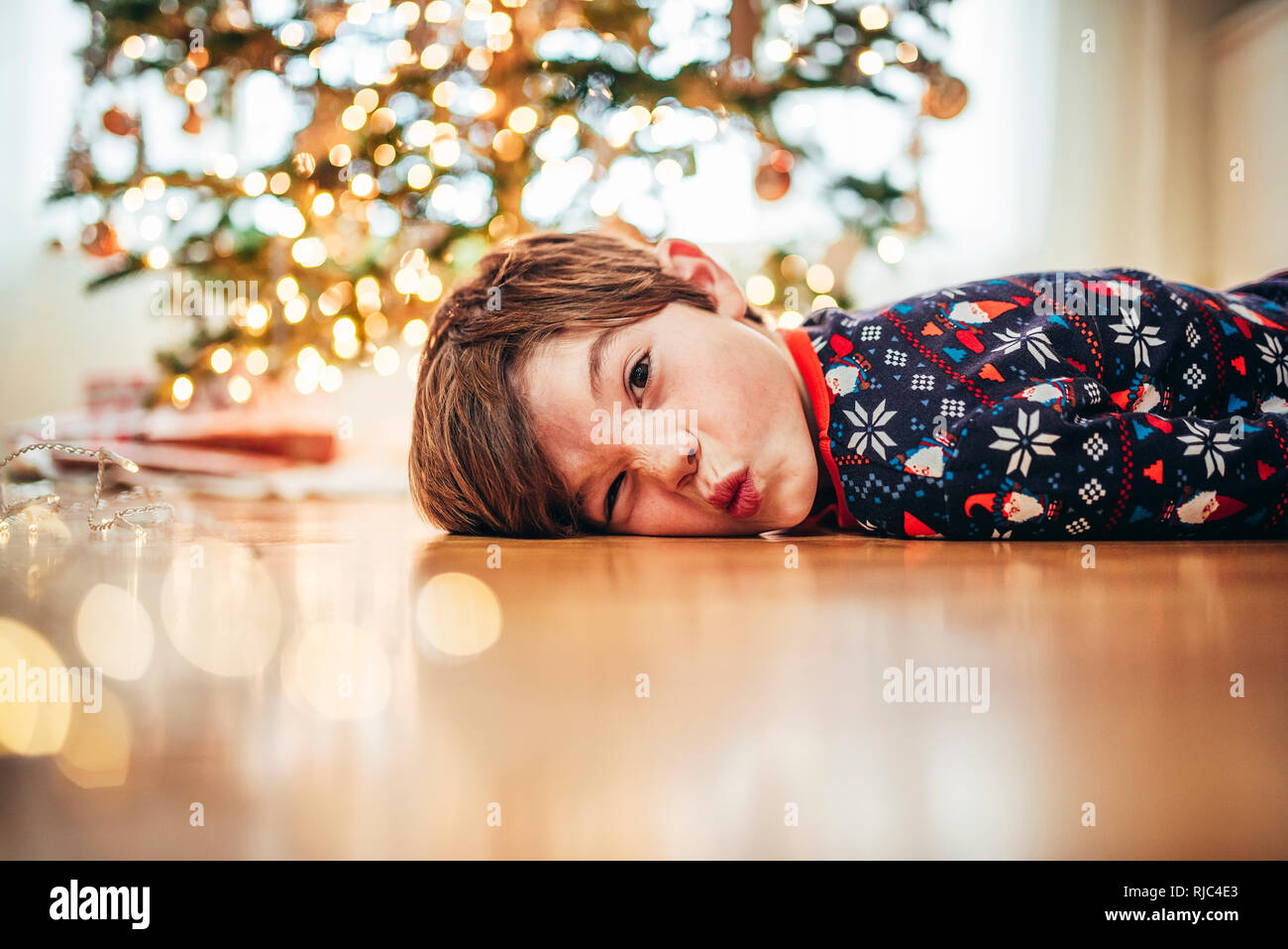Junge lag auf dem Boden vor einem Weihnachtsbaum lustige Gesichter ziehen Stockfoto