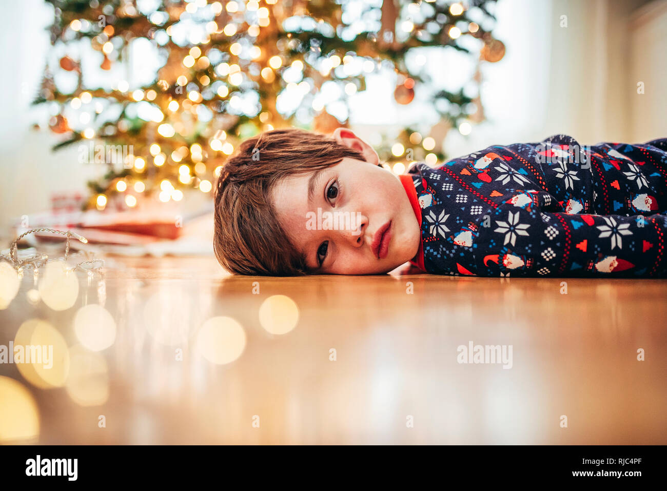 Junge lag auf dem Boden vor einem Weihnachtsbaum Stockfoto