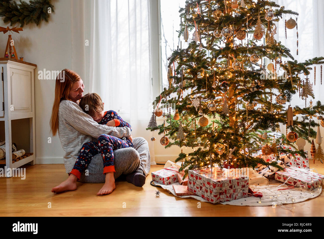 Frau sitzt mit einem Weihnachtsbaum ihr Sohn umarmen Stockfoto