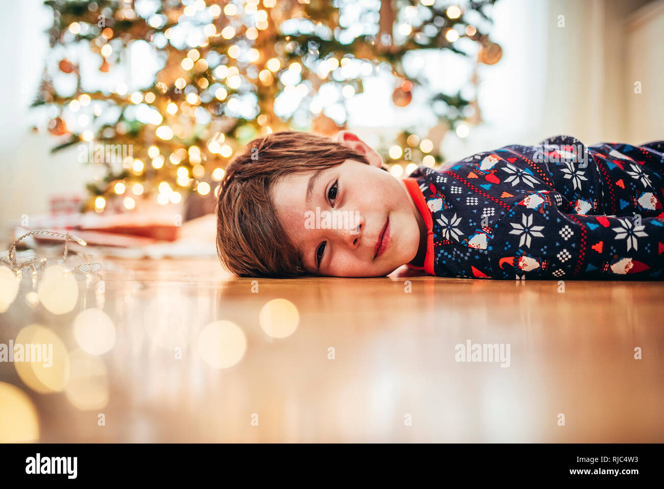 Lächelnde Junge lag auf dem Boden vor einem Weihnachtsbaum Stockfoto