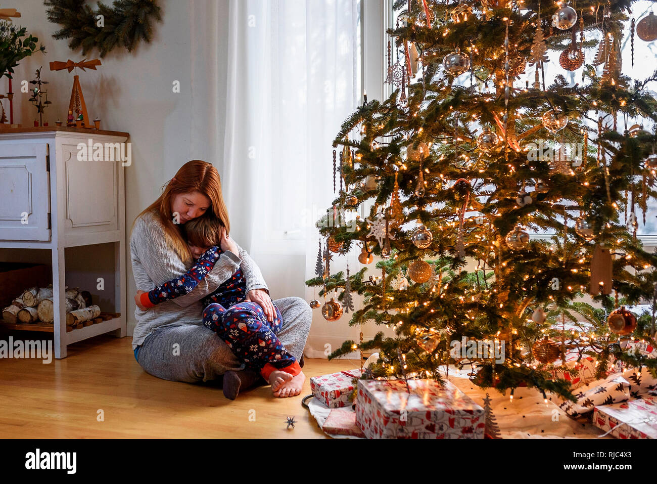 Frau sitzt mit einem Weihnachtsbaum ihr Sohn umarmen Stockfoto