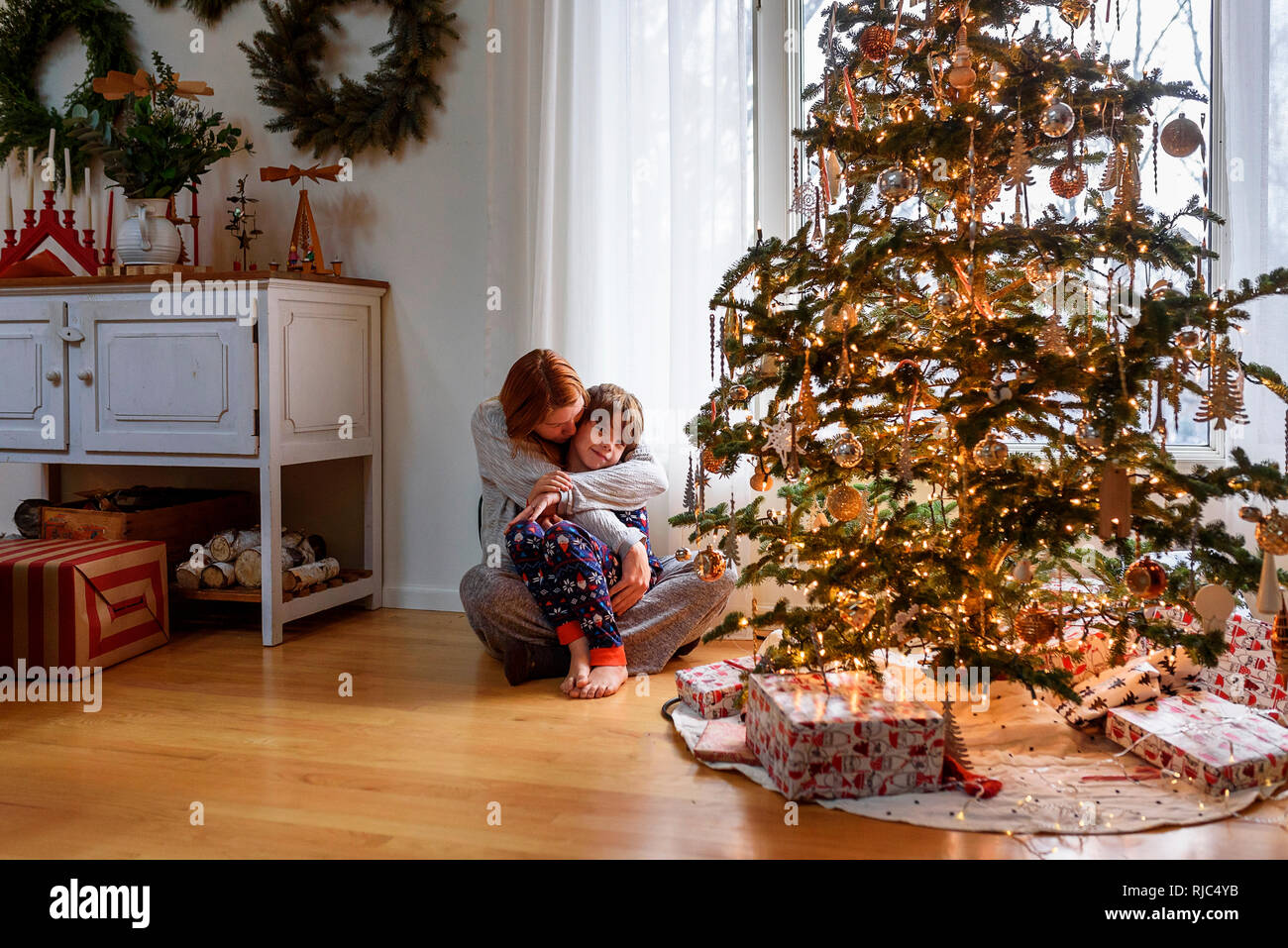 Frau sitzt mit einem Weihnachtsbaum ihr Sohn umarmen Stockfoto