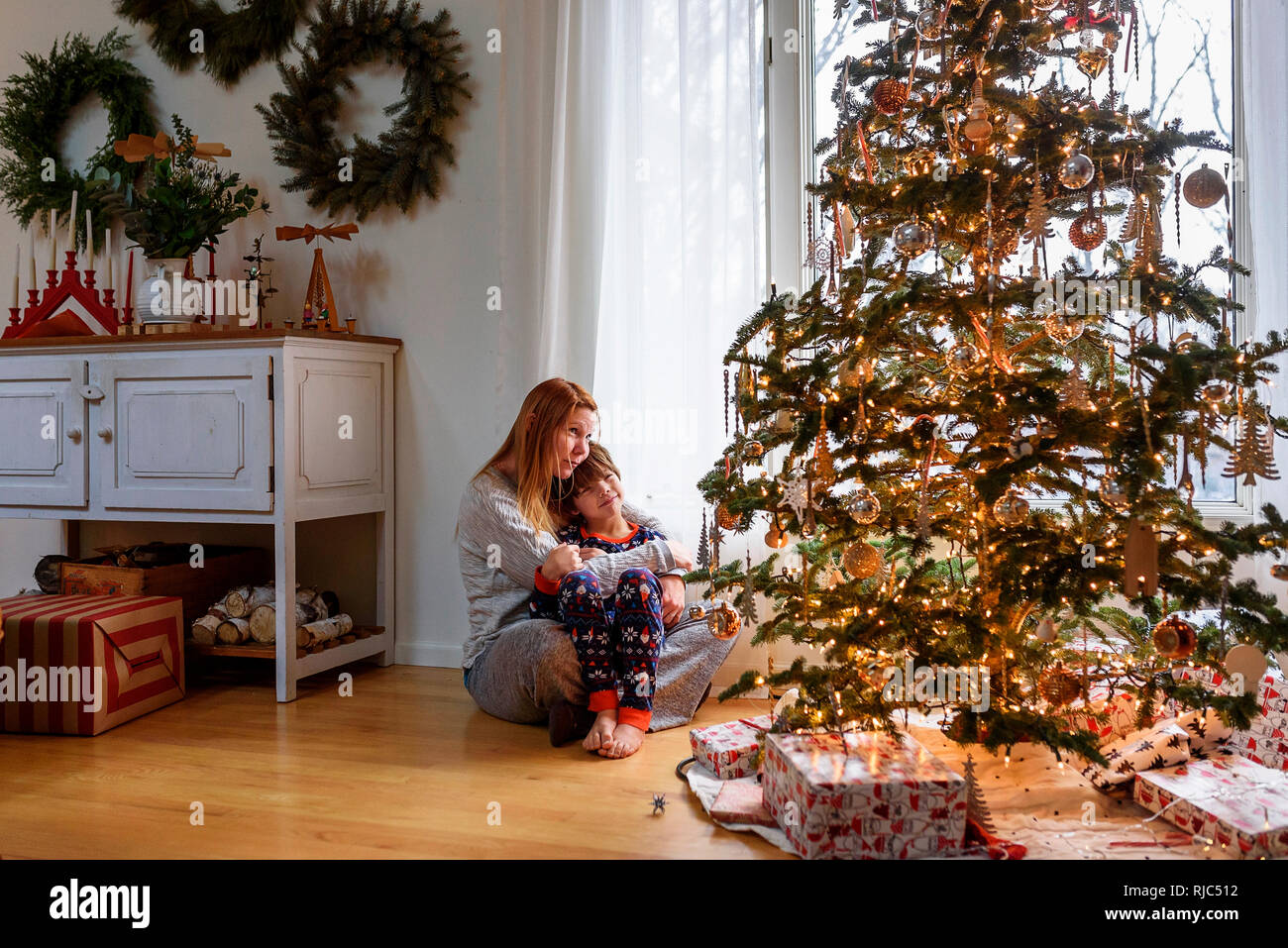Frau sitzt mit einem Weihnachtsbaum ihr Sohn umarmen Stockfoto