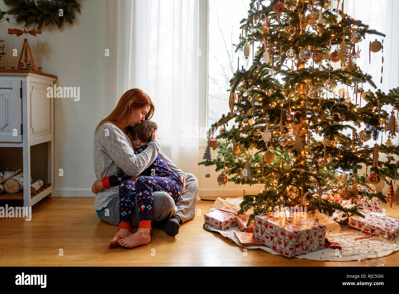 Frau sitzt mit einem Weihnachtsbaum ihr Sohn umarmen Stockfoto