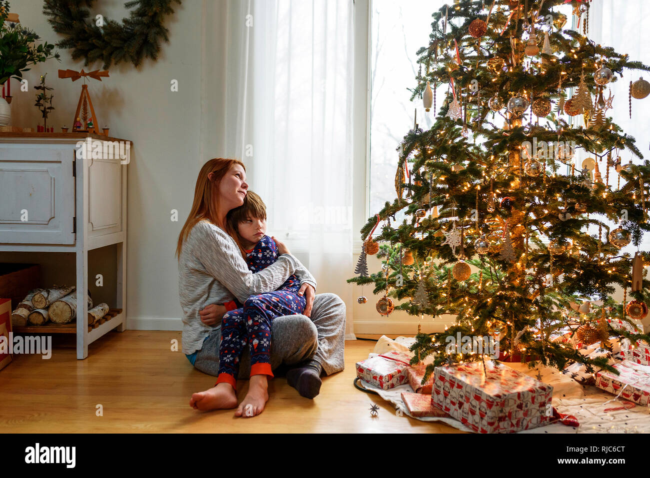 Frau sitzt mit einem Weihnachtsbaum ihr Sohn umarmen Stockfoto