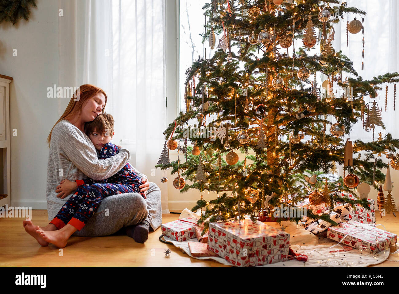 Frau sitzt mit einem Weihnachtsbaum ihr Sohn umarmen Stockfoto