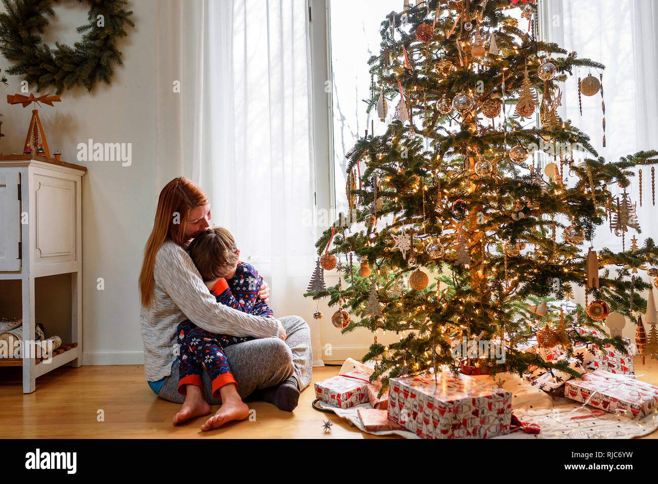 Frau sitzt mit einem Weihnachtsbaum ihr Sohn umarmen Stockfoto