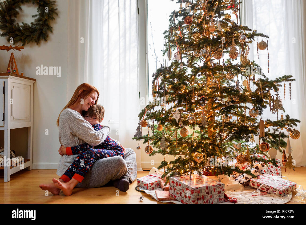 Frau sitzt mit einem Weihnachtsbaum ihr Sohn umarmen Stockfoto