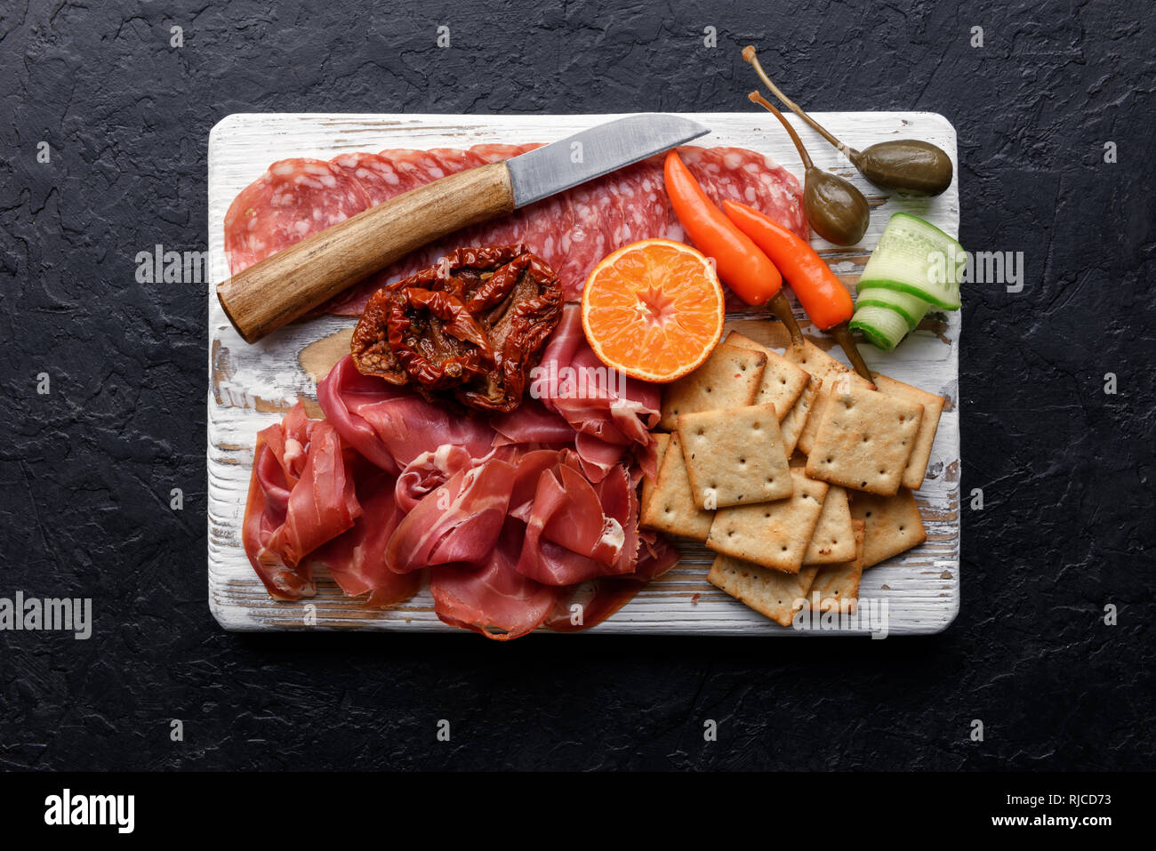Italienische Antipasti Snacks. Kapern, Prosciutto, Salami und Cracker über Schwarz grunge Tabelle, Ansicht von oben. Essen Fotografie Stockfoto
