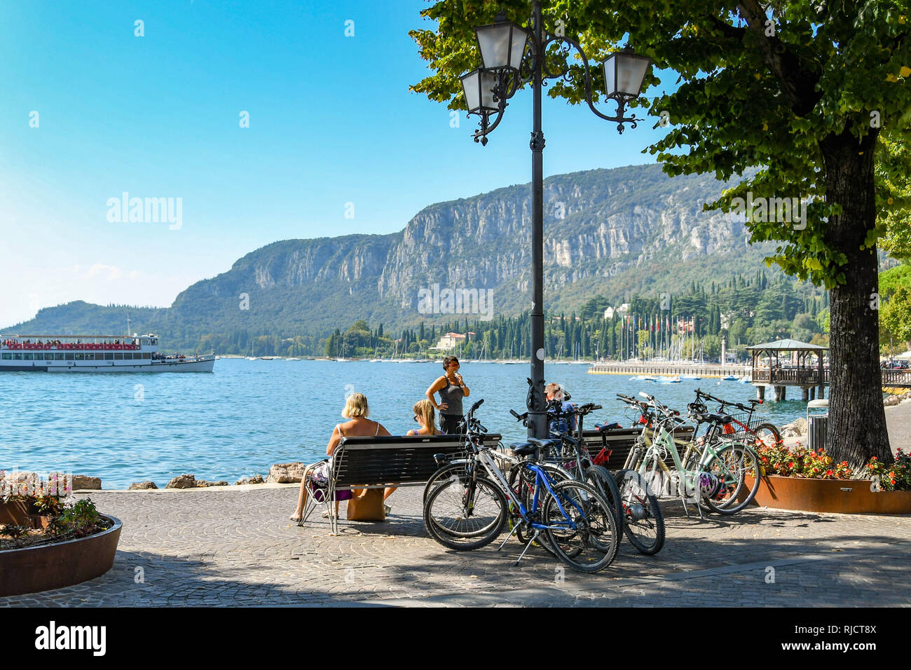 GARDA, Gardasee, Italien - September 2018: Menschen sitzen auf der Seite des Gardasees mit Fahrrädern neben geparkt. Stockfoto